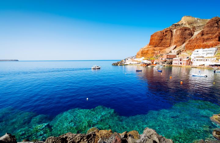 a body of water with boats and buildings on the side amoudi bay Santorini