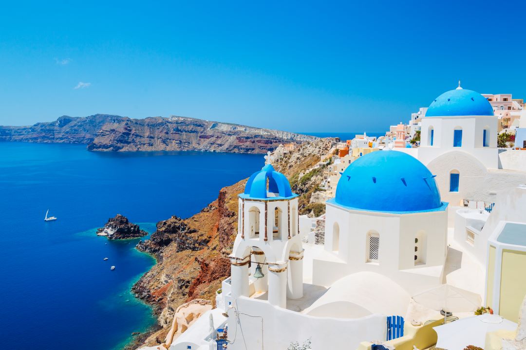 3 blue domes of Oia Santorini with blue Aegean Sea in backgraound
