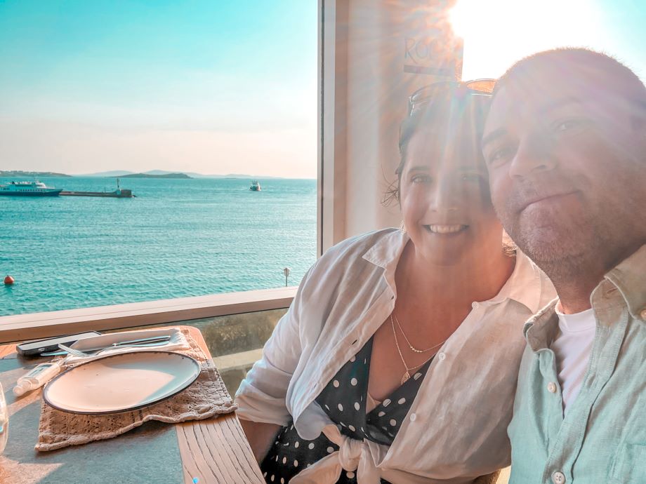 Couple dining at Roca Sunset with the sun setting in the background over the Aegean Sea