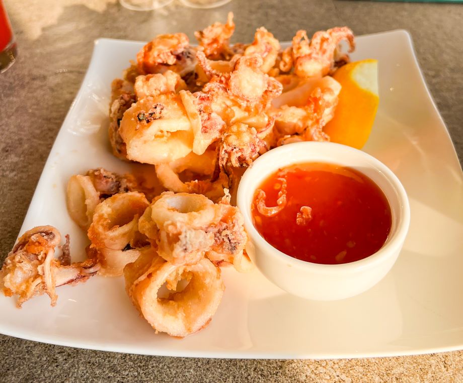 Roca Sunset fried Calamari on white plate with sweet chili dipping sauce in a bowl.