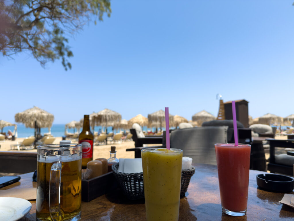 Drinks including a passionfruit smoothie at Sirokos Taverna with Episkopi Beach in the background