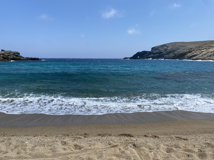 a beach with a body of water and hills emote Mykonos beaches Fokos Beach