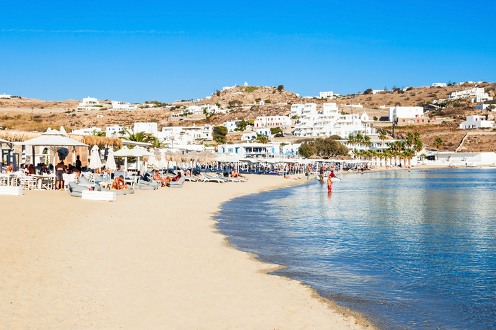 a beach with people and umbrellas and water Ornos beach on the Mykonos island, Cyclades in Greece