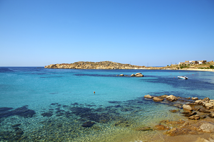 a body of water with rocks and a hill in the background Paraga Beach Mykonos beaches