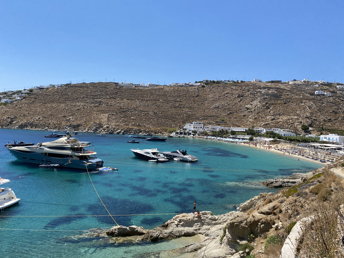 boats in a bay with boats and buildings in the background View of Psarou Beach in Mykonos, Greece