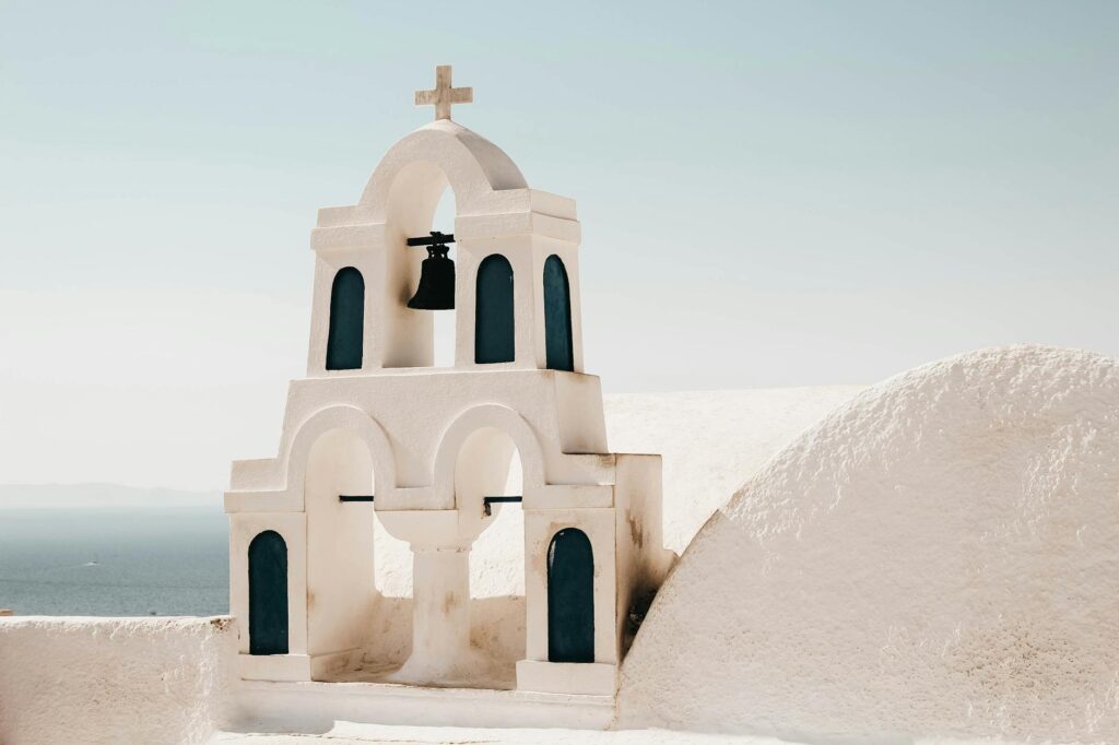 a white Santorini Greece church tower with a cross and a bell