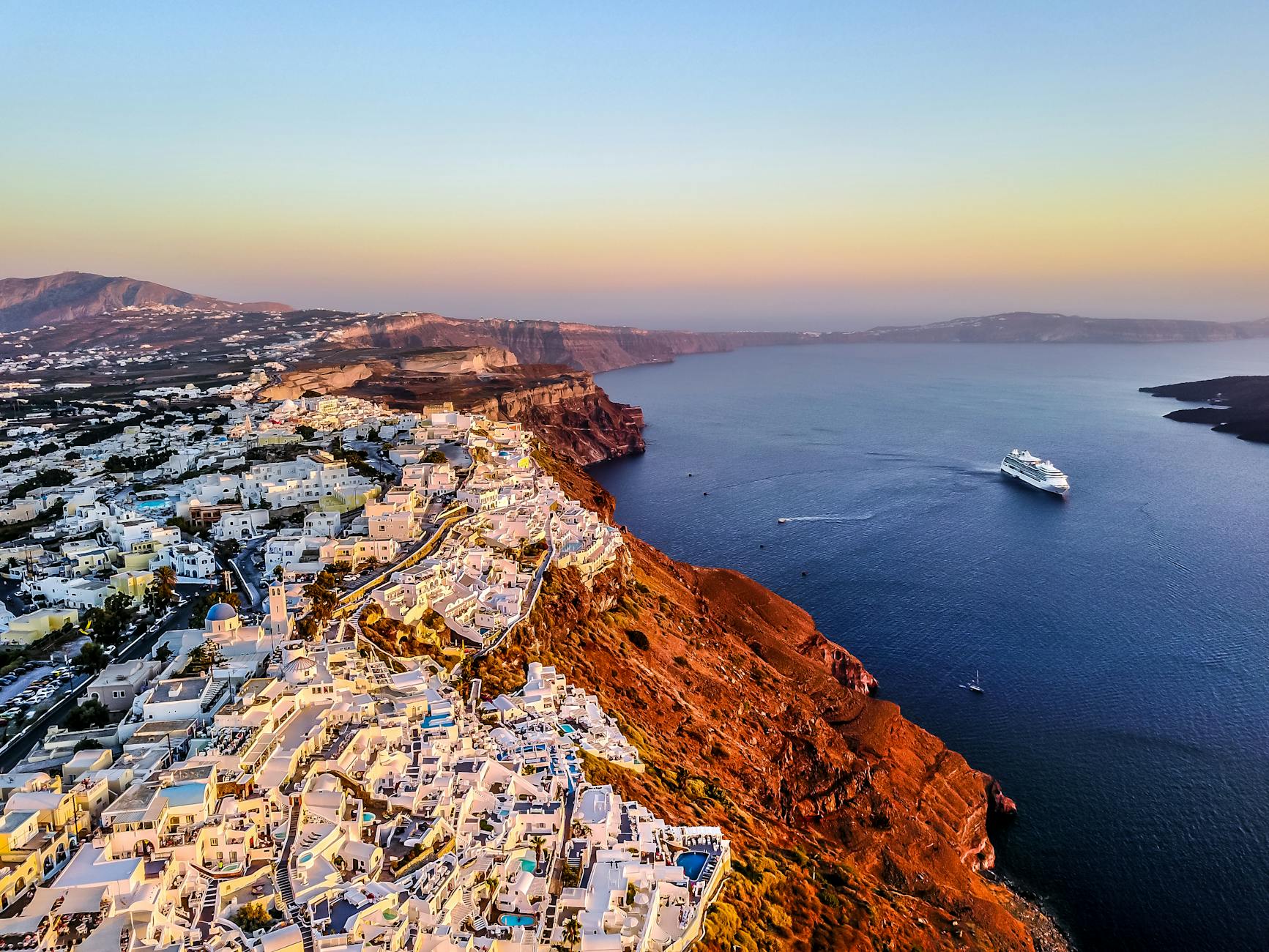 From Athens to Santorini white buildings on a cliff by the water in Santorini Greece during sunset