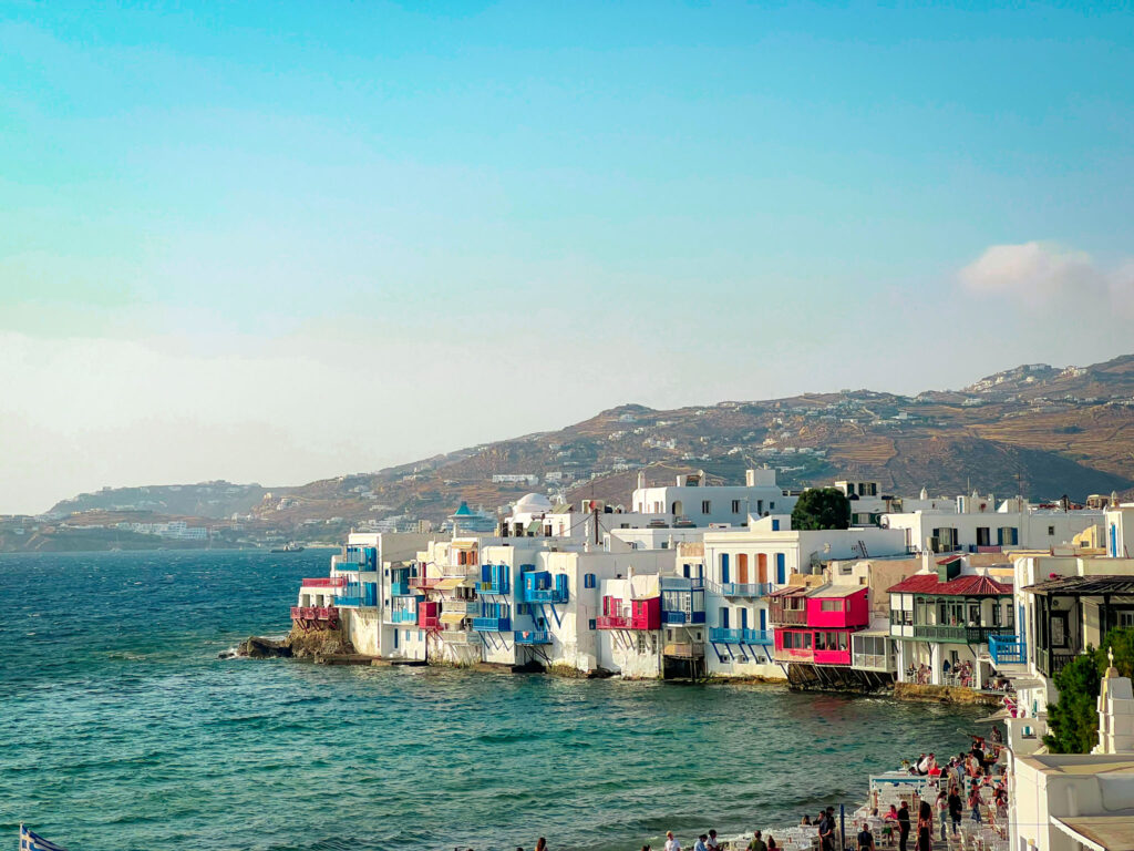 a group of people walking on a beach Little Venice Mykonos Greece