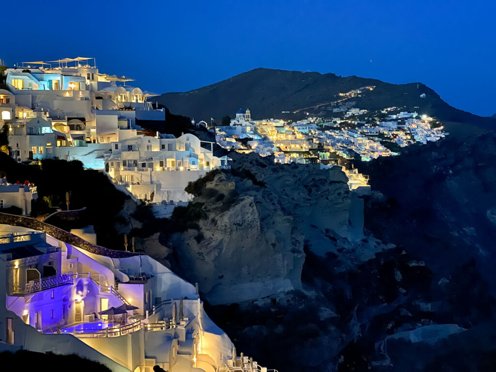 a lit up buildings on a mountain Santorini Caldera at night