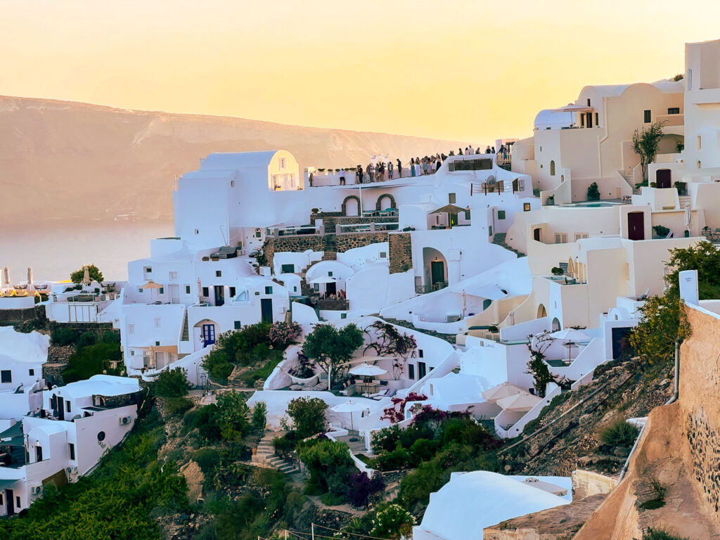 a group of people walking on a hill with white buildings Santorini Caldera