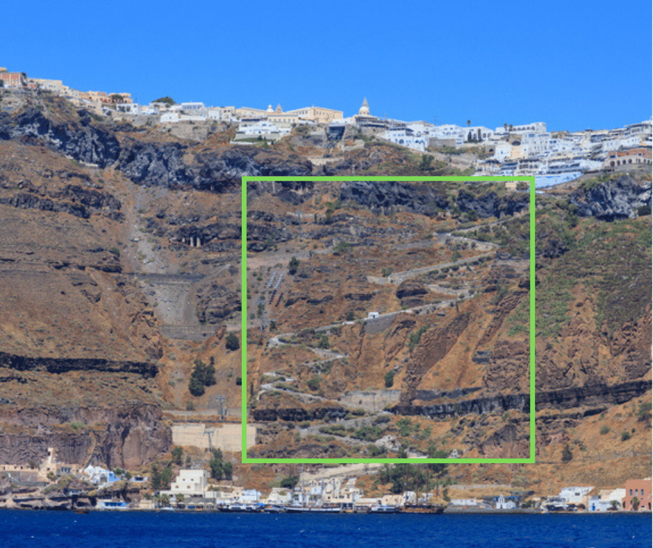Steep zigzagging trail with donkeys and walkers climbing the rocky cliffs from the old port to Fira in Santorini, with whitewashed buildings lining the top of the caldera. The rugged terrain highlights one of the more adventurous routes that may raise the question, “is Santorini safe” for all travelers.