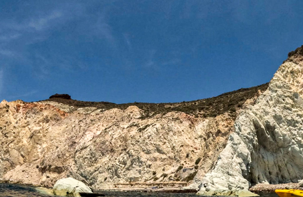 a rocky cliff with a body of water and blue sky