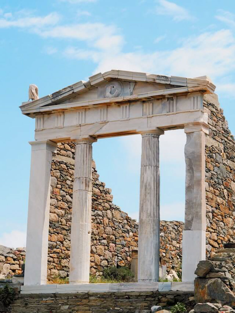 A close-up of a well-preserved marble doorway framed by tall columns and stacked stone walls behind, showcasing classic Delian architecture.